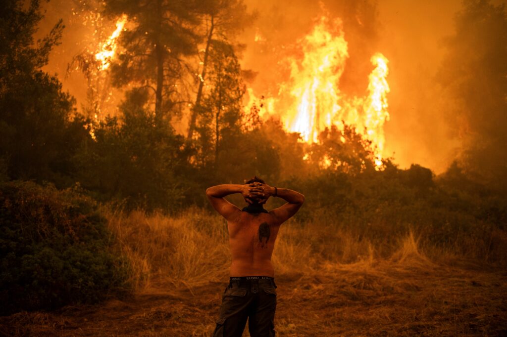 A local resident reacts to a large blaze during an attempt to extinguish forest fires approaching the village of Pefki on Evia island, Greece's second largest island, on Aug. 8, 2021. Credit: Angelos Tzortzinis/AFP via Getty Images