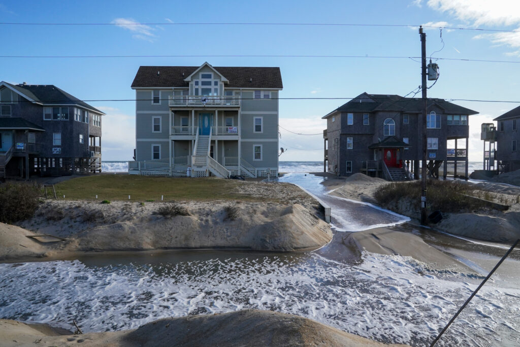 Waves from the Atlantic Ocean wash past houses to flood Seagull Street on the Outer Banks of North Carolina in December 2022 in Rodanthe, N.C. Dare County agreed to abandon the street and allowed all 12 houses on the strip to be collectively moved from the encroaching ocean. Credit: Jahi Chikwendiu/The Washington Post via Getty Images
